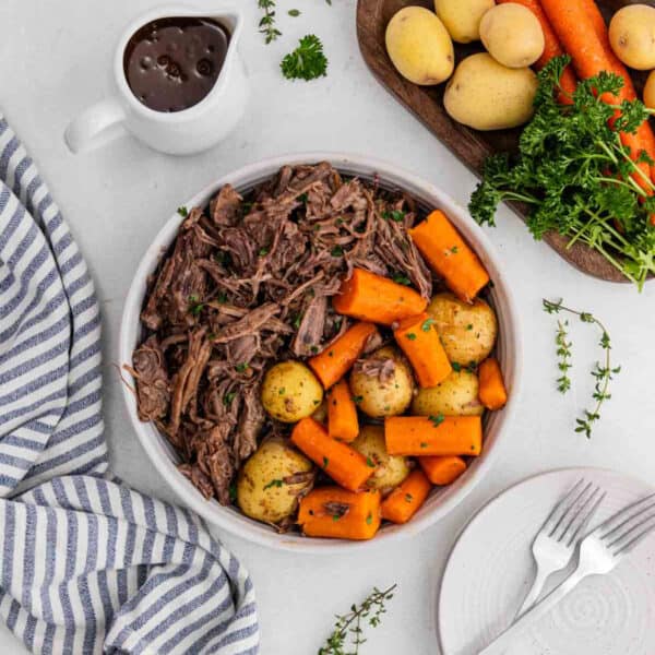 Shredded roast in a bowl with potatoes and carrots.