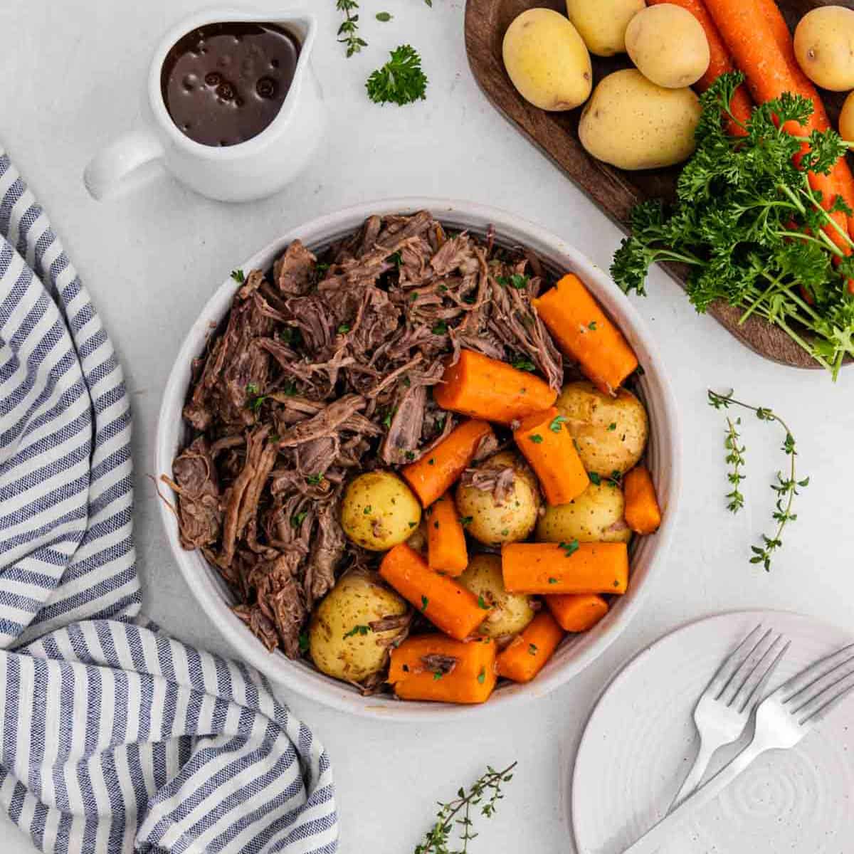 Shredded roast in a bowl with potatoes and carrots.