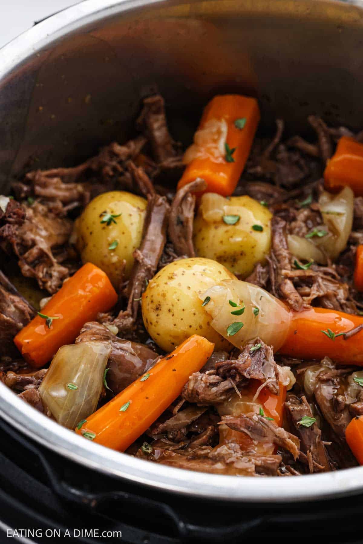 Cooked shredded roast, potatoes and carrots in the instant pot topped with gravy.