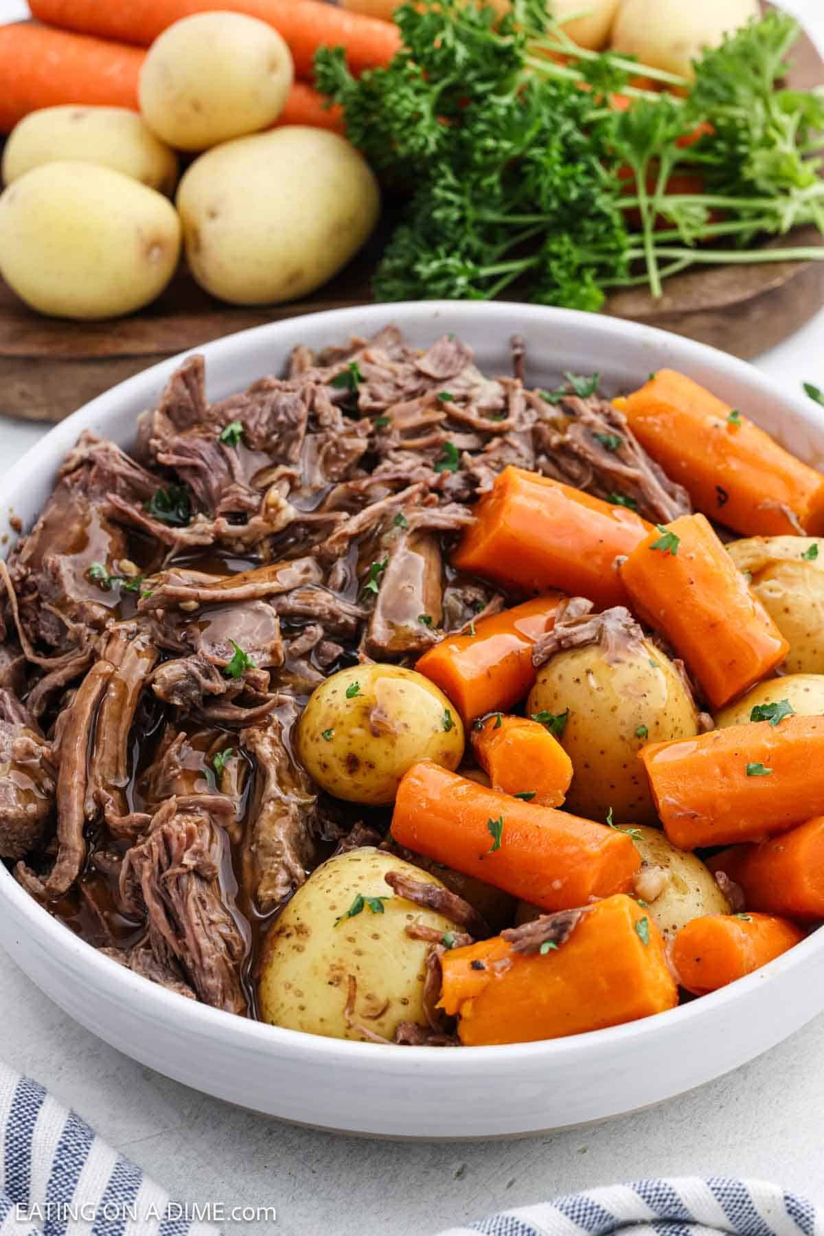 Shredded cooked roast in a bowl with carrots and potatoes topped with gravy.