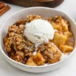 Apple crisp recipe topped with ice cream in a bowl.