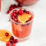 A small glass of pink punch topped with cranberries and orange slices.