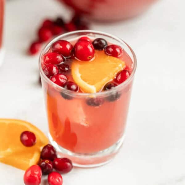 A small glass of pink punch topped with cranberries and orange slices.