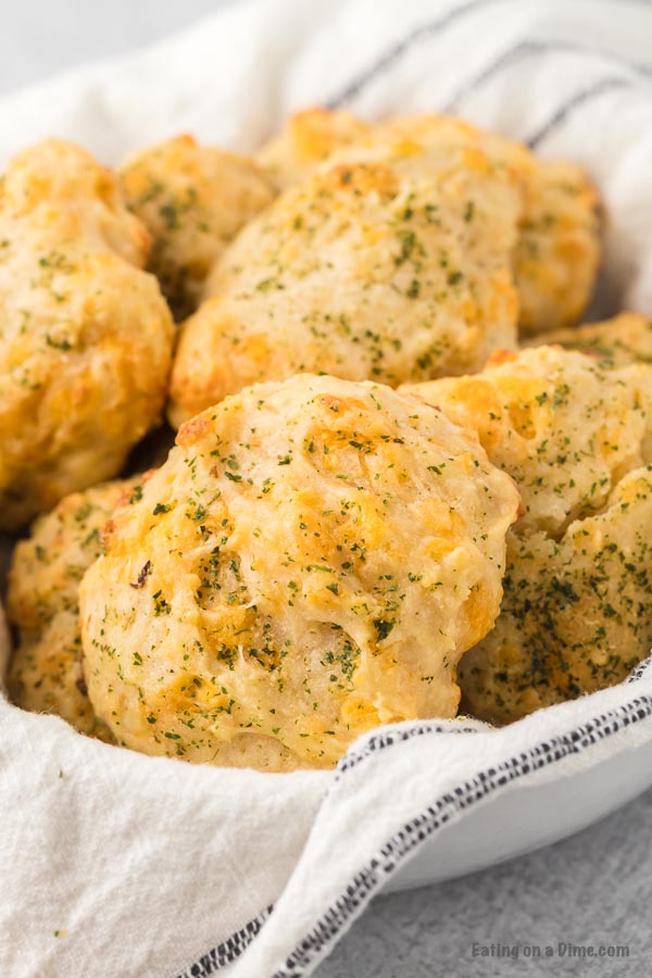 Close up image of cheddar bay biscuits in a bowl with a kitchen towel. 