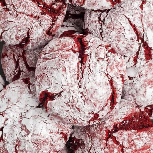 Close-up of several red velvet crinkle cookies, coated in powdered sugar with cracked surfaces revealing the red cookie underneath—an irresistible treat from a classic Red Velvet Cookies Recipe.