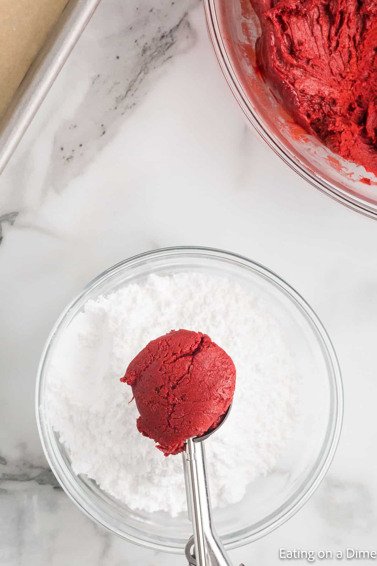 Red velvet cookie dough on cookie scoop over a bowl of powdered sugar