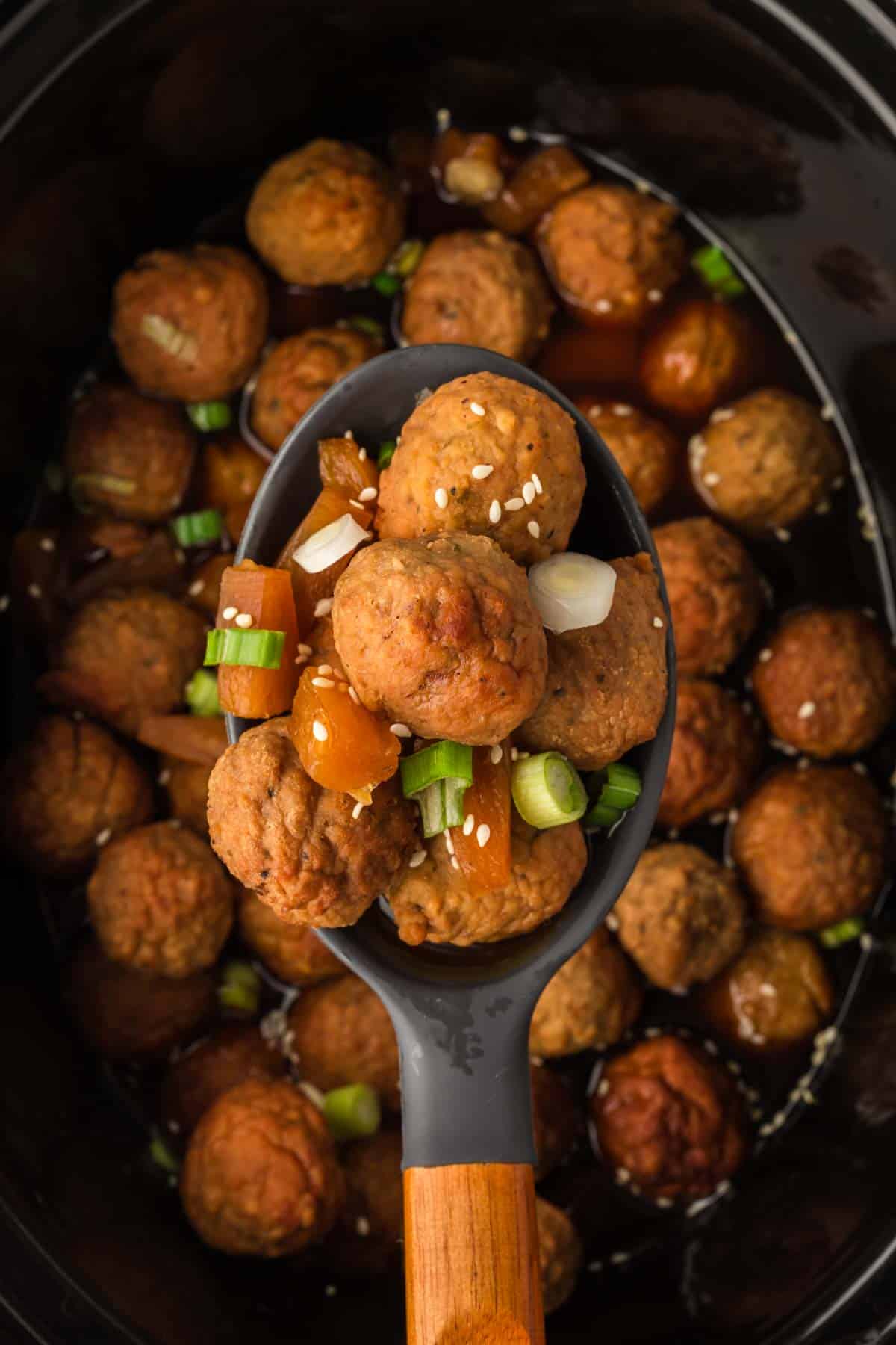 Close up image teriyaki meatballs in the slow cooker with a serving on a spoon
