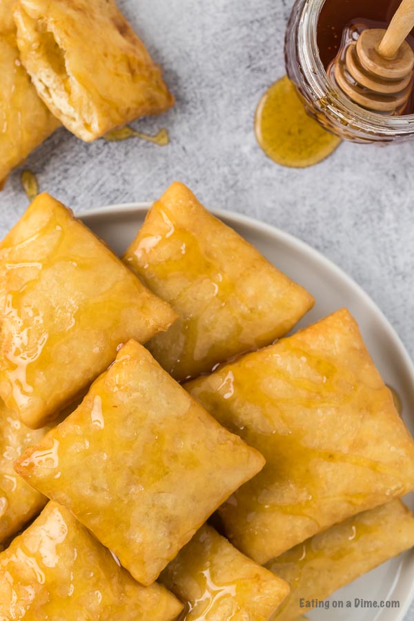 Close up image of sopapillas drizzled with honey on a white plate. 