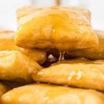 Close-up of golden, square sopapillas covered in honey syrup, with one beignet elevated above the rest and honey dripping from its corner.