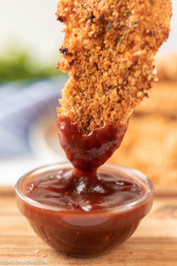 The breaded chicken strip being dipped into the BBQ sauce 