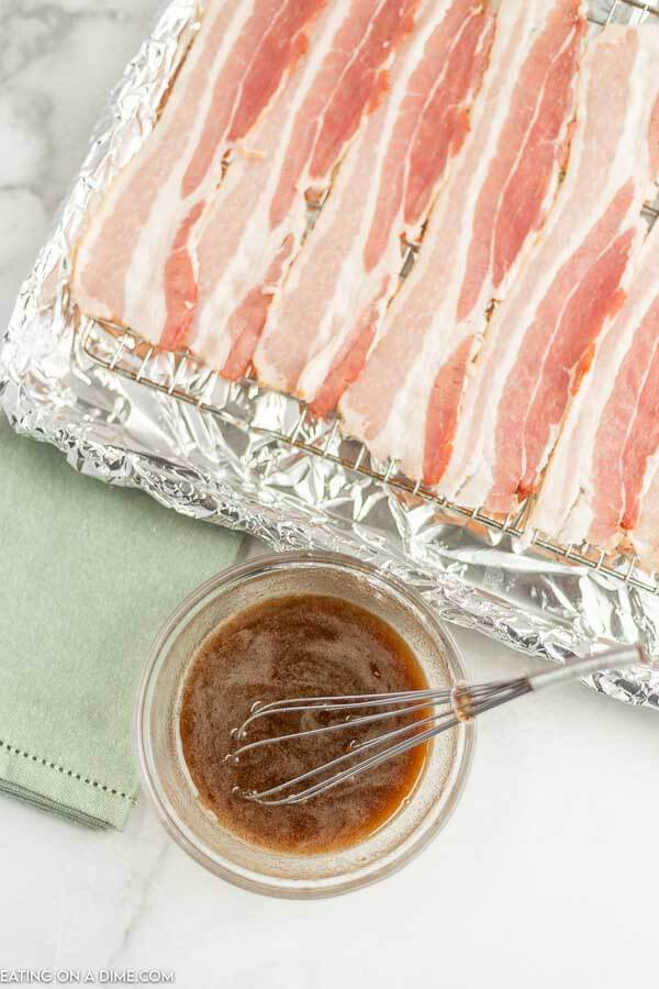Bacon on a lined baking sheet beside a bowl of brown sugar and syrup. 