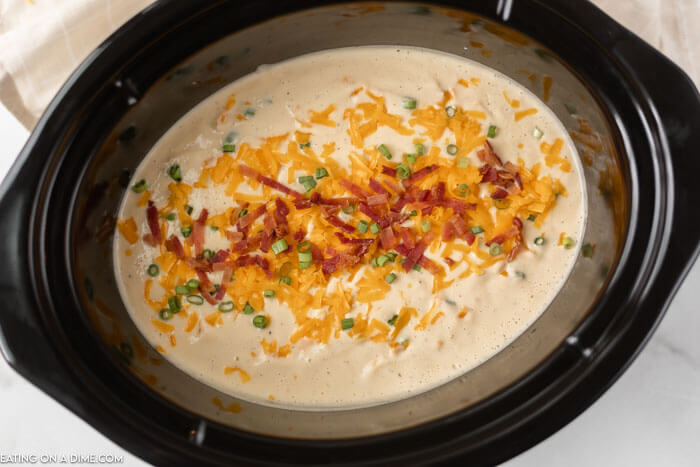 Crock pot full of cauliflower soup topped with shredded cheese and bacon.