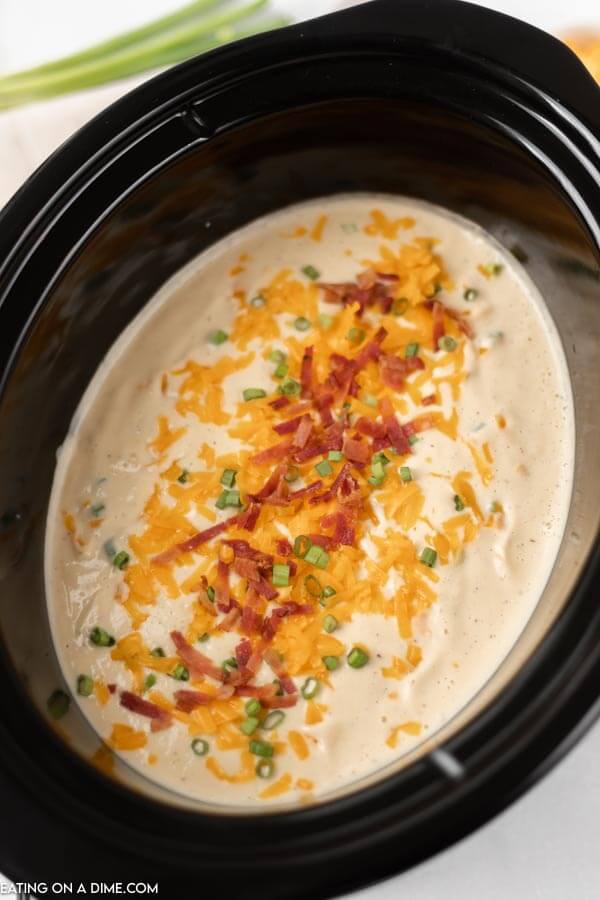 Crock pot of cauliflower soup topped with cheese, bacon and green onion. 