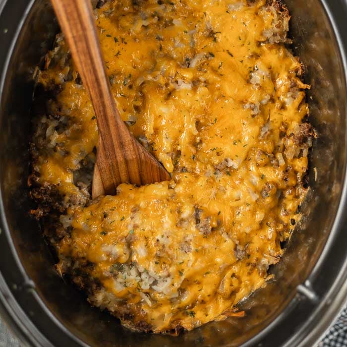 Close up image of Hamburger Casserole in the crock pot with a wooden spoon. 