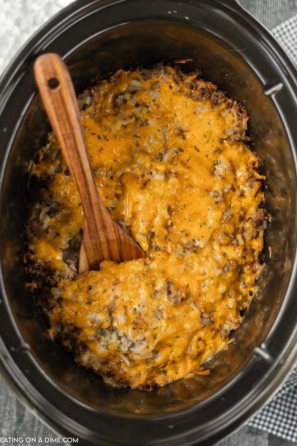 Close up image of Hamburger Casserole in the crock pot with a wooden spoon. 