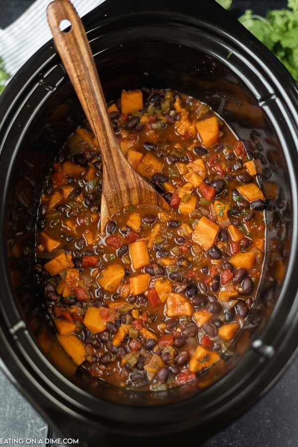 Close up image of sweet potato black bean chili with a wooden spoon in the crock pot. 