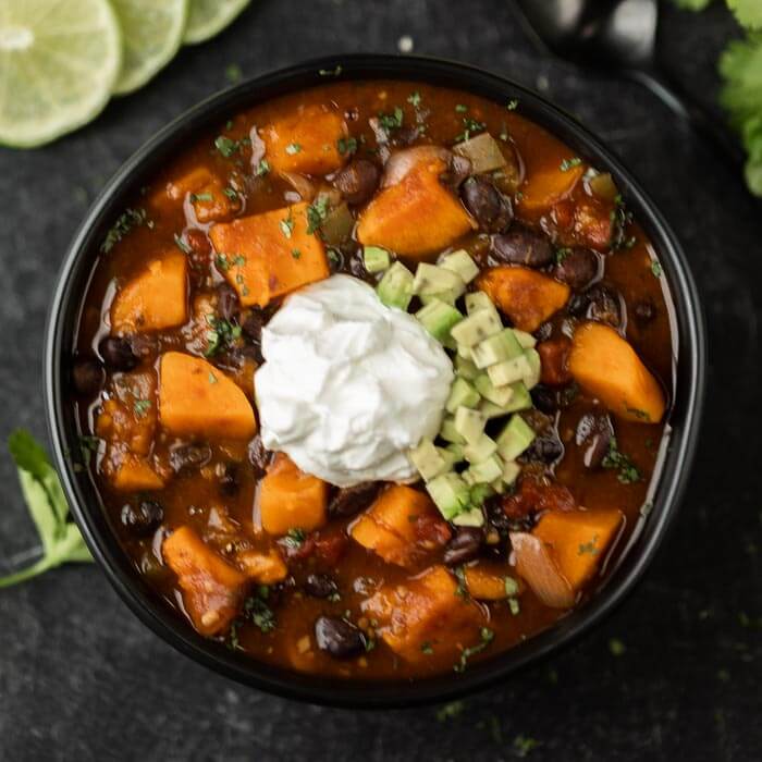 Close up image sweet potato black bean chili with sour cream and avocado on top. 