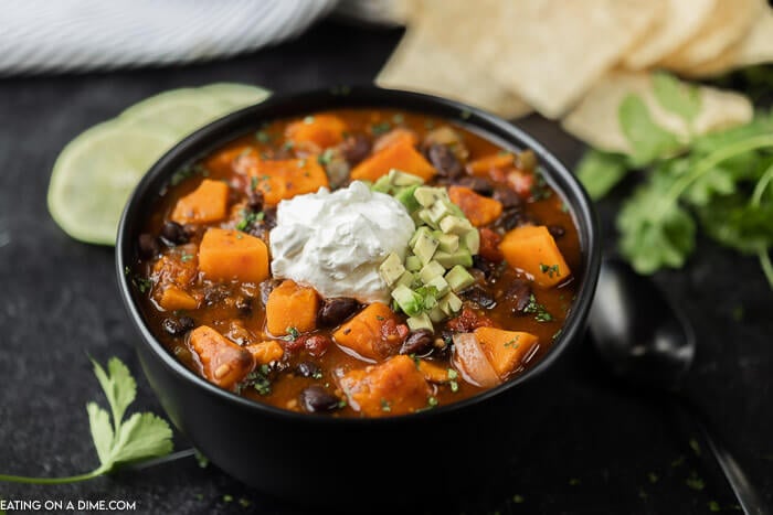 Close up image of sweet potato black chili in a black bowl with sour cream and diced avocado on top. 