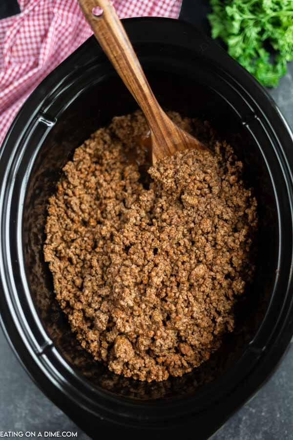 close up image of taco meat in the crock pot with a wooden spoon. 