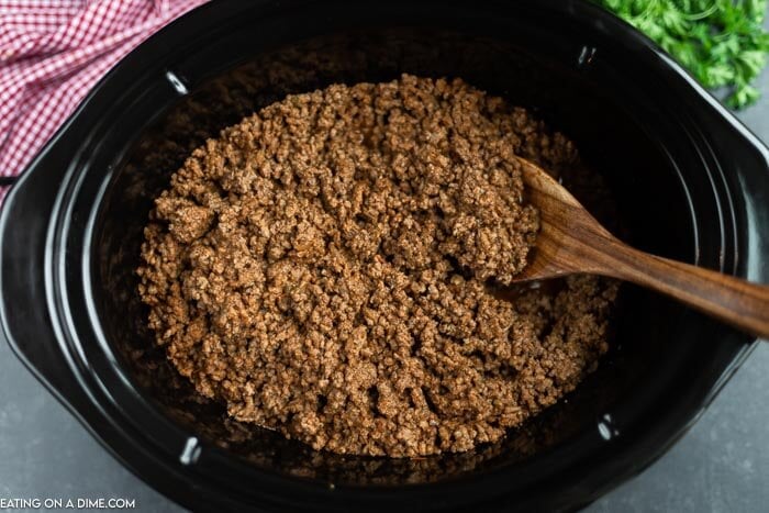 Close up image of taco meat in the crock pot with a wooden spoon. 