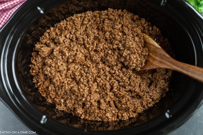 Close up image of taco meat in the crock pot with a wooden spoon. 