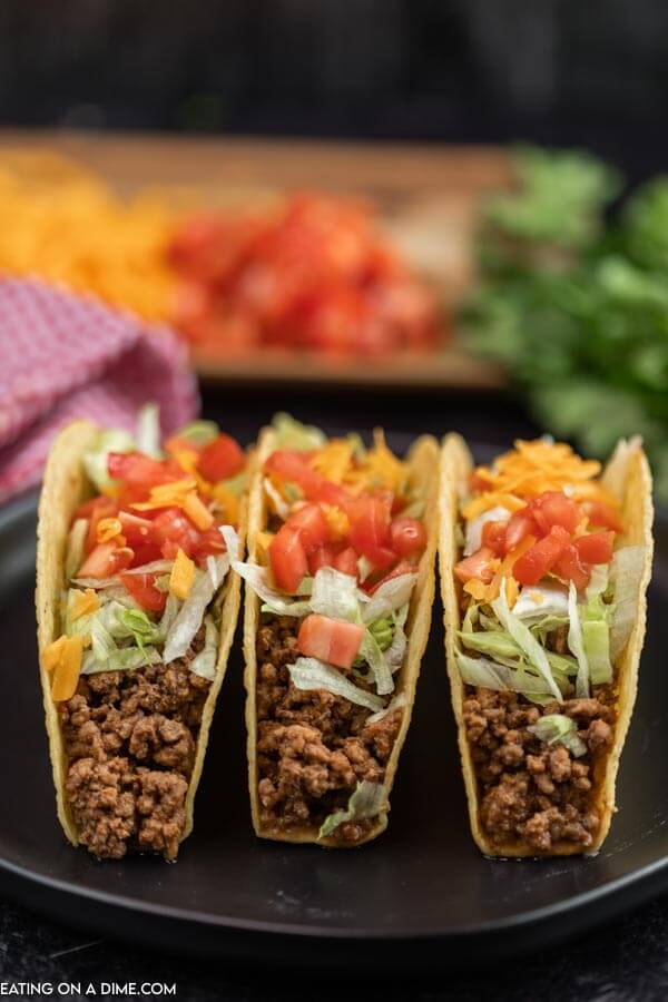 Close up image of three tacos on a plate topped with lettuce, cheese and tomatoes. 