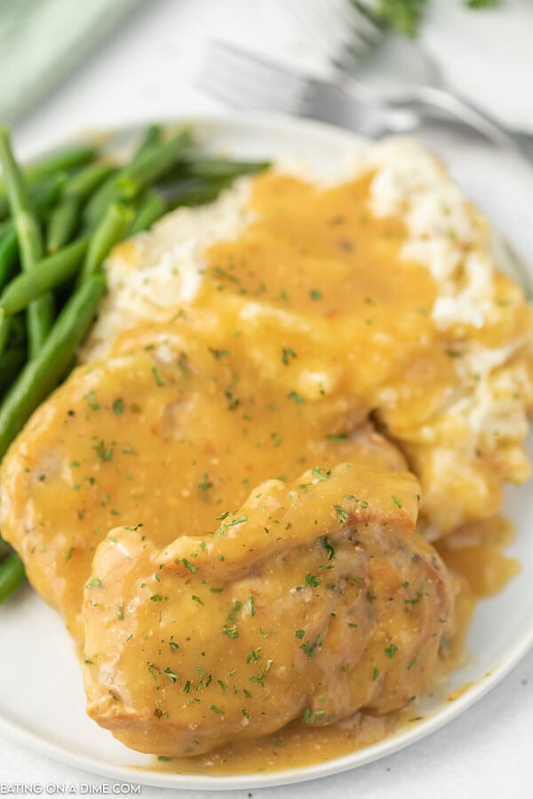 Close up image of pork chops and gravy with a side of mashed potatoes and green beans.