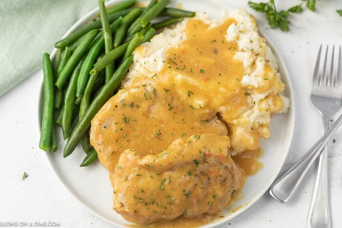 Close up image of pork chops and gravy with a side of mashed potatoes and green beans.