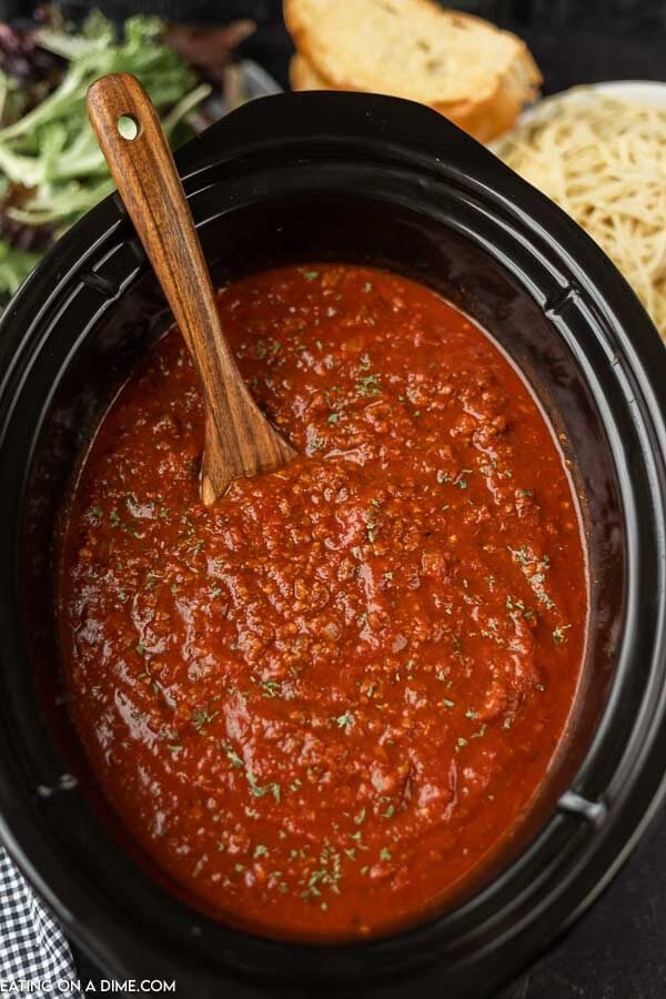Close up image of spaghetti sauce in the crock pot with a wooden spoon. 