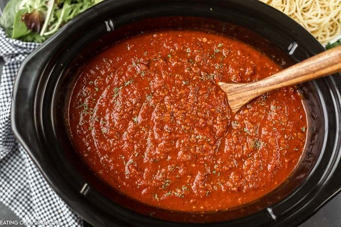 Close up image of spaghetti sauce in the crock pot with a wooden spoon in the sauce. 