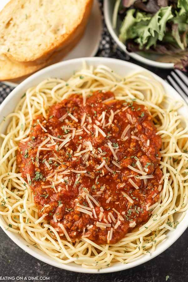 Close up image of a spaghetti with sauce on top on a white plate with a side of french bread and salad. 