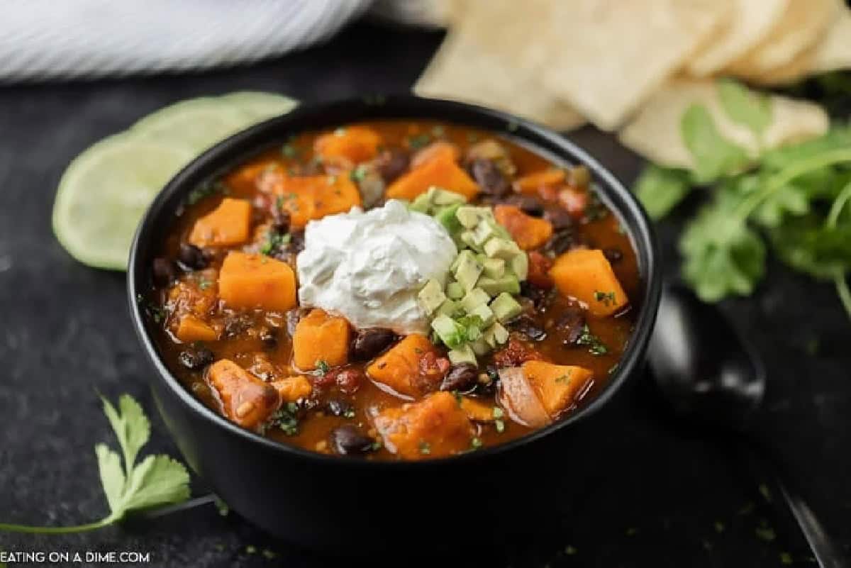 Crock Pot Sweet Potato Black Bean Chili is the perfect meal to serve on Meatless Monday or any day of the week. This chili is hearty and delicious. Close up image of sweet potato black chili in a black bowl with sour cream and diced avocado on top.