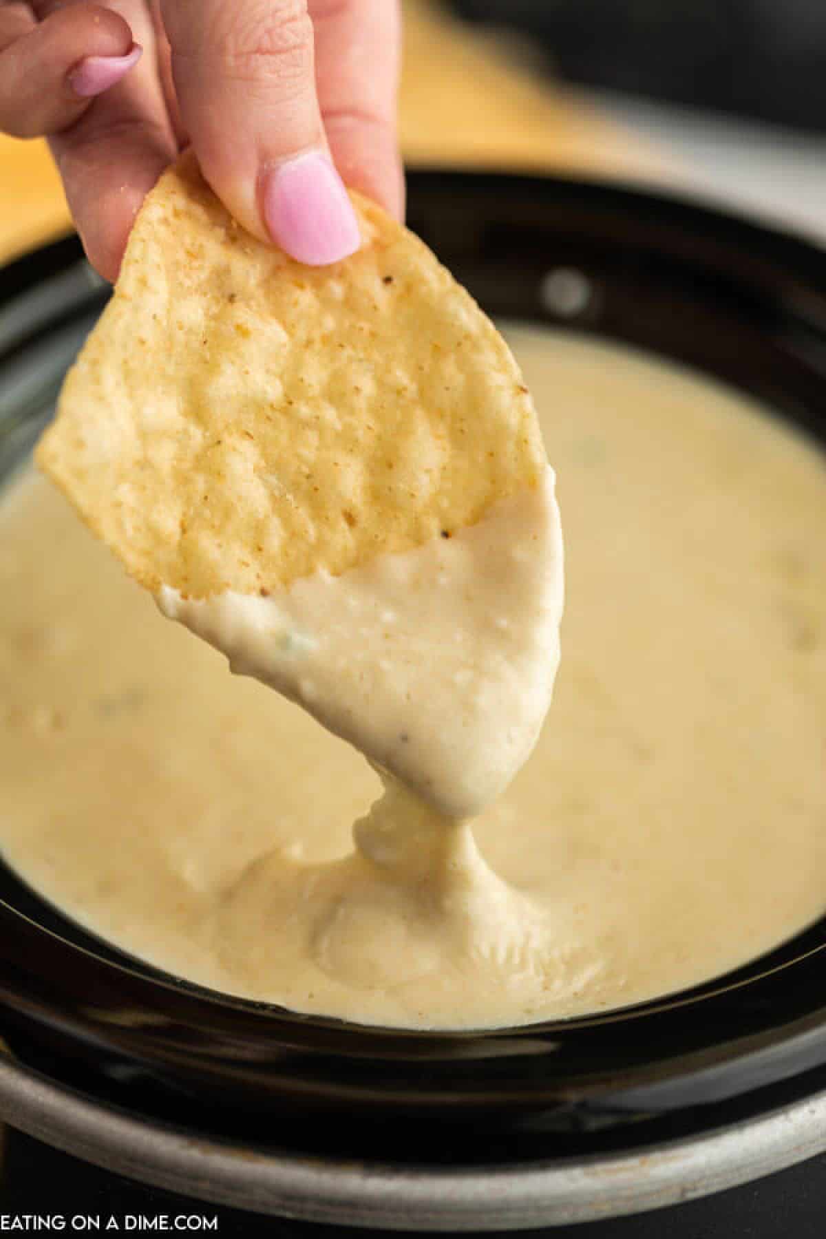 A chip dipping into the white cheese dip in a crock pot 
