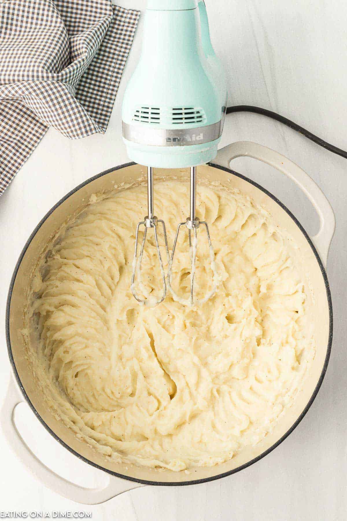 Mashing potatoes in a large pot with a hand mixer