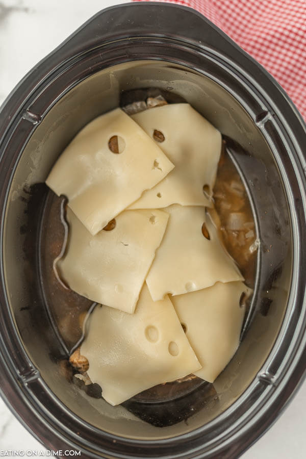 close up image of french onion chicken topped with cheese in the crock pot. 