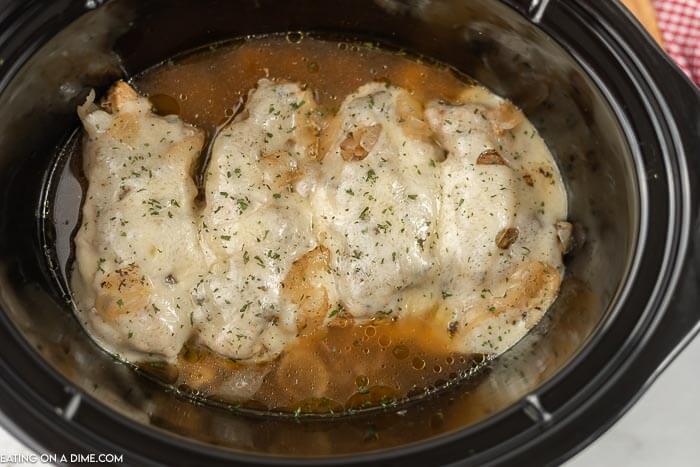 close up image of french onion chicken in the crock po topped with cheese. 