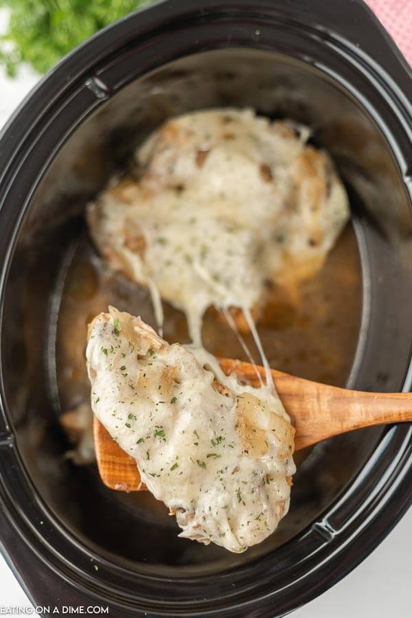 close up image of french onion chicken in the crock pot with a serving a wooden spoon