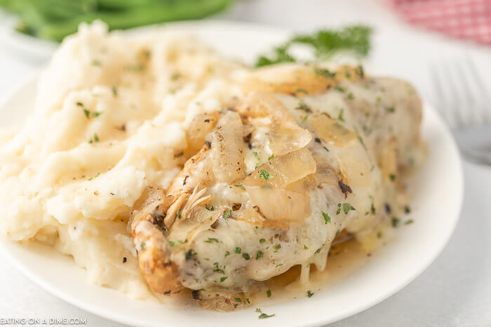 Close up image of french onion chicken on a white plate with mashed potatoes. 