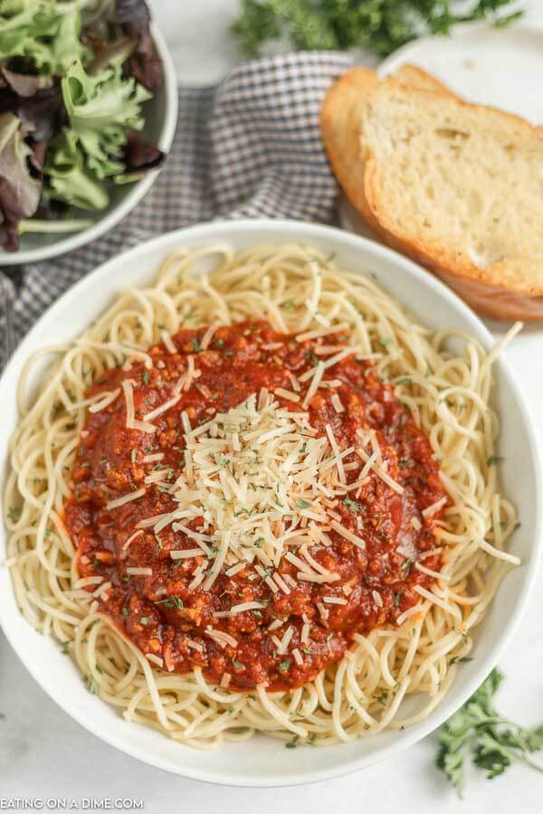 Close up image of a plate of spaghetti and sauce with a side of salad and bread. 