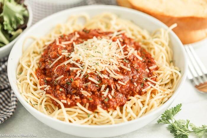 close up image of spaghetti and sauce in a white bowl with parmesan cheese on top.