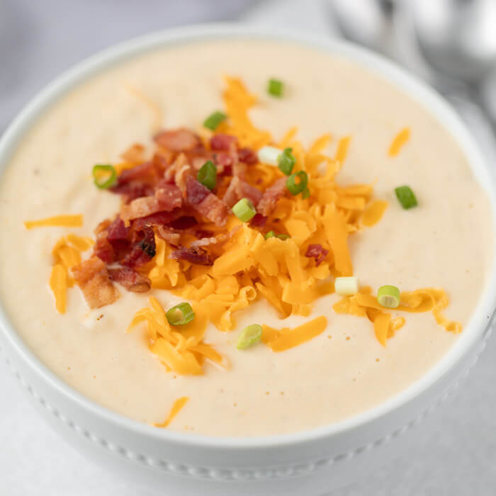 Close up image of cauliflower soup topped with cheese, bacon and onion in a white bowl. 