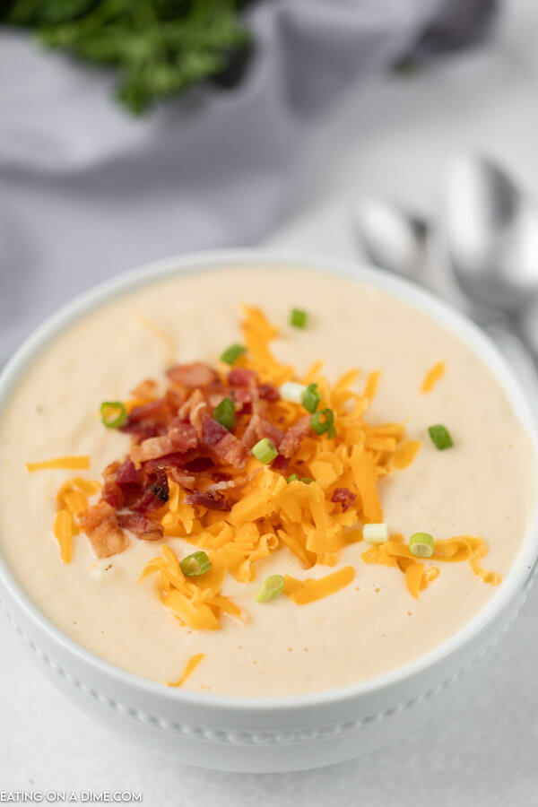 Close up image of cauliflower soup topped with cheese, bacon and onion in a white bowl. 