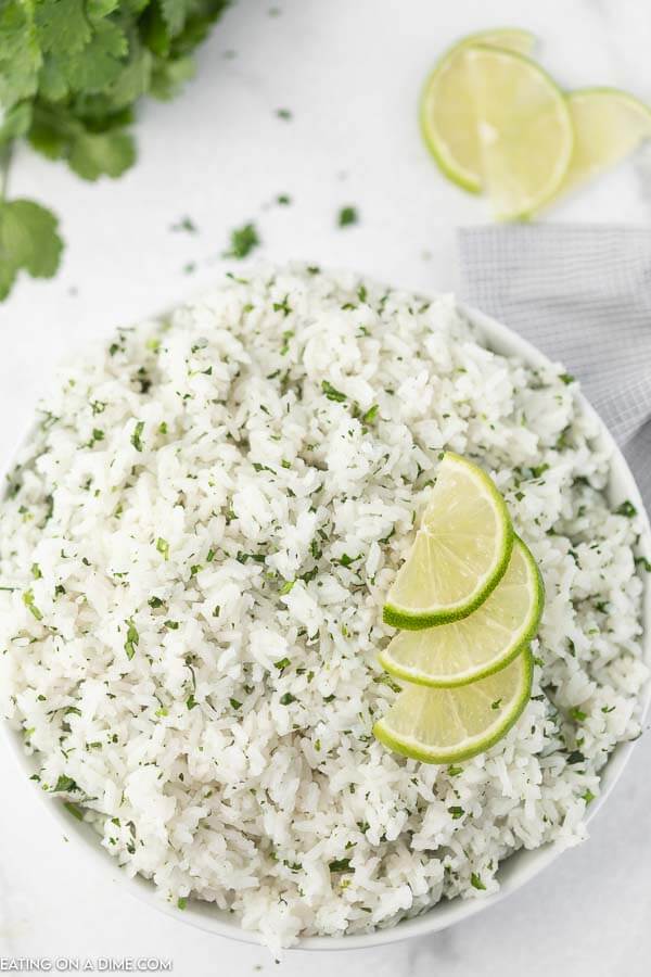 Close up image of a bowl of cilantro lime rice with slice limes on top. 
