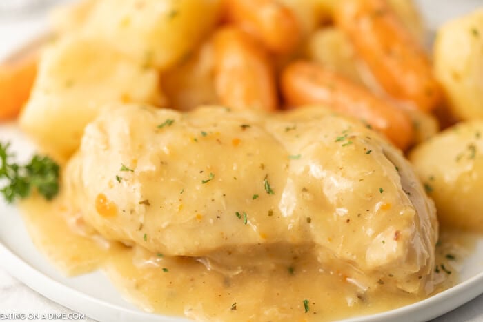 Close up image of creamy chicken ranch on a white plate with a side of potatoes and carrots. 