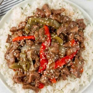 Pepper steak with red bell peppers over rice on a plate.