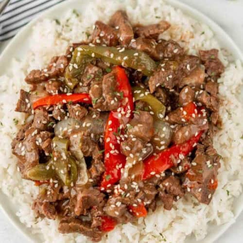 Pepper steak with red bell peppers over rice on a plate.