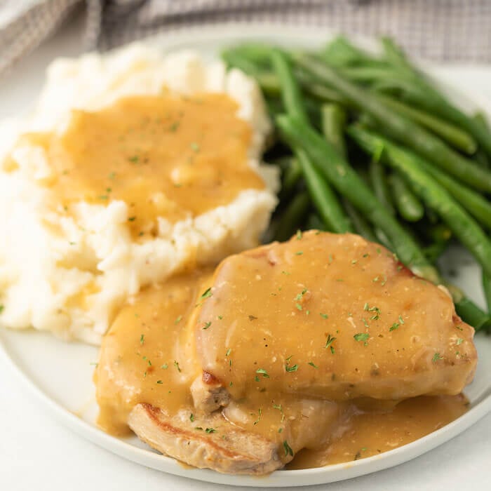 Plate of pork chops with gravy and mashed potatoes and green beans. 