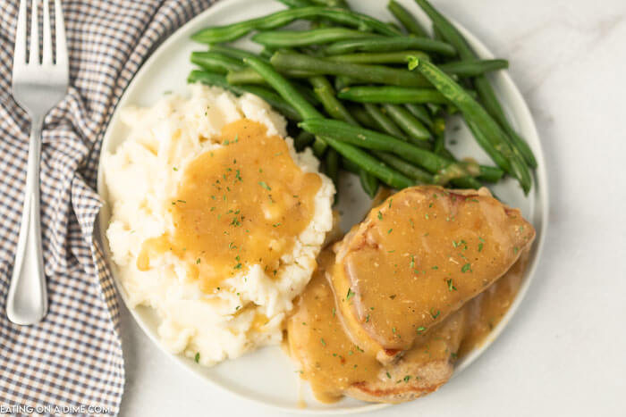 Plate of pork chops with gravy and mashed potatoes and green beans. 
