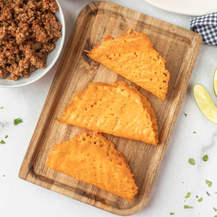 Close up image of keto taco shells on a cutting board with a side of hamburger meat