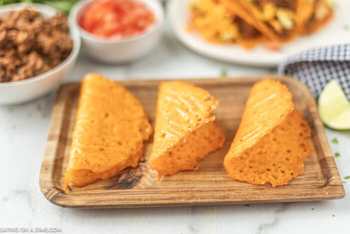 Close up image of keto taco shells on a cutting board with a side of hamburger meat, tomatoes. 